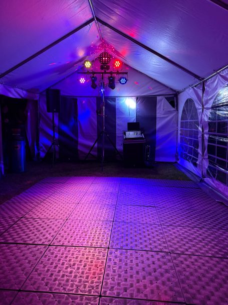 Leerer Veranstaltungszelt mit bunten Lichtern und einer DJ-Anlage im Hintergrund.