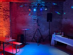 Ein Partyraum mit bunten Lichtern, Lautsprecher und einer Getränketheke.
