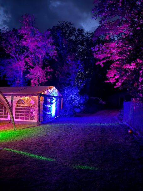 Beleuchteter Garten mit einem Zelt und bunten Lichtern in der Nacht.