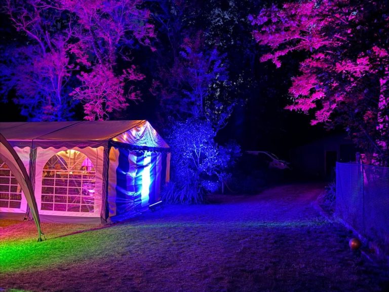 Beleuchteter Garten mit einem Zelt und bunten Lichtern in der Nacht.