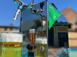 Zwei Gläser Bier stehen neben einem glänzenden Zapfhahn im Freien.