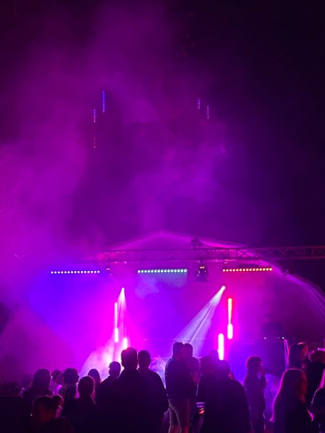 Lichtershow mit bunten Lichtern und Nebel, Menschen tanzen davor.